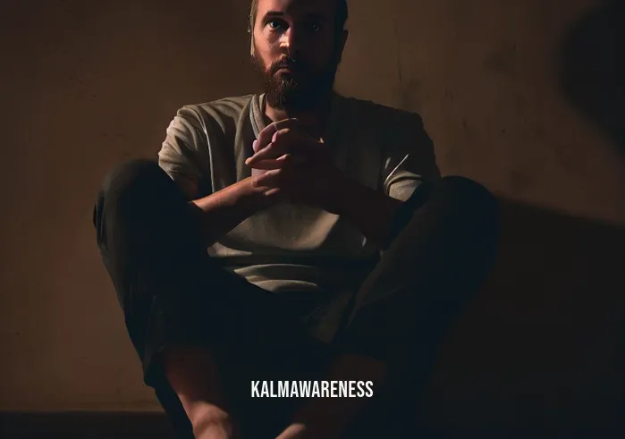 letting go of fear meditation _ Image: A person sitting alone in a dimly lit room, their face filled with anxiety and fear.Image description: A dimly lit room with a single individual sitting cross-legged on the floor, hands resting on their knees, and a troubled expression on their face.