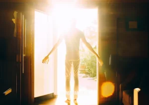 morning guided meditation for energy _ Image: The person stands tall, full of vitality, as they exit their home into the bright morning sunshine, ready to embrace the day ahead.Image description: With renewed energy, they step outside, prepared for whatever challenges may come their way.